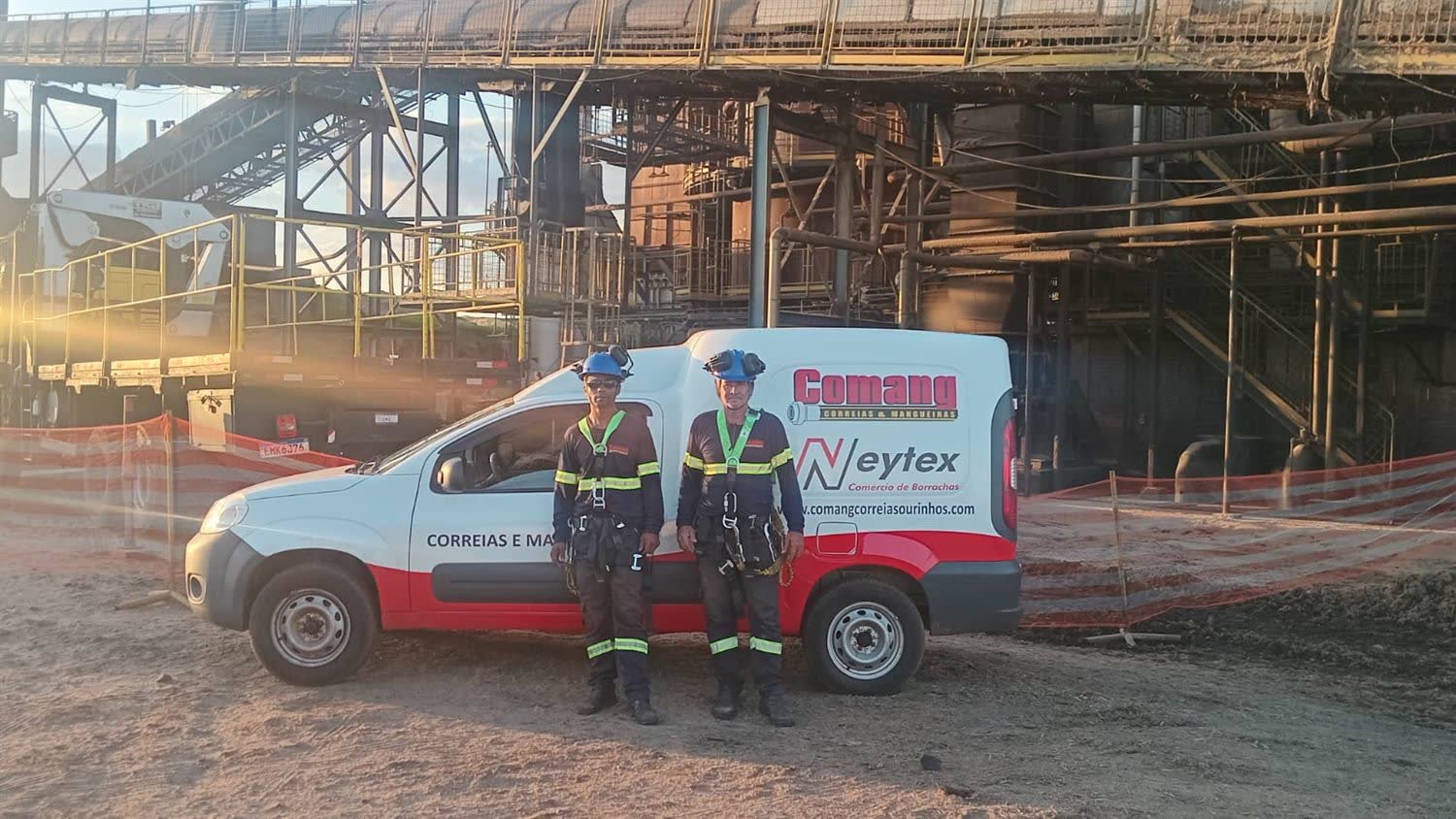 Equipe técnica da Comang, de capacete e cinto de segurança, em frente ao veículo da empresa dentro de uma planta industrial